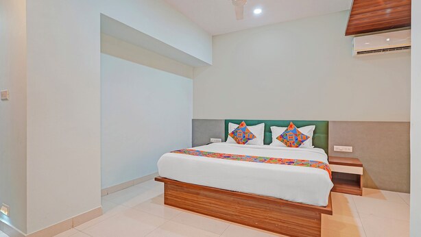 A modern bedroom with a wooden bed frame, a green upholstered headboard, and a colorful geometric-patterned bedspread. - FabHotel New Mysore Gate (Bengaluru)