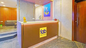 A hotel reception area with a wooden reception desk, a sofa, a mirror, and a painting on the wall. - FabHotel New Mysore Gate (Bengaluru)