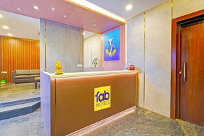 A hotel reception area with a wooden reception desk, a sofa, a mirror, and a painting on the wall. - FabHotel New Mysore Gate (Bengaluru)