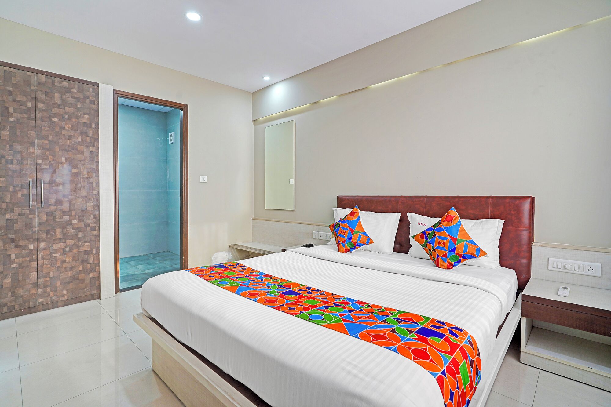 A modern hotel room with a large bed, a wardrobe, a bathroom, and a nightstand.