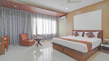 A hotel room with a large bed, a wooden headboard, a ceiling fan, and a window with patterned curtains.