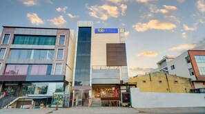 A modern building with a 'fab hotels' sign, featuring a glass facade and a ground-level retail space. - Fabhotel Pride Image (Bangalore)
