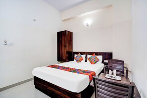 A hotel room with a bed, a wooden wardrobe, a small table with a tray, and a chair. - Fabhotel Pride Image (Bangalore)