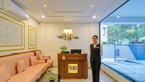 A hotel reception area with a sofa, a reception desk, a chandelier, and a view of the outside. - Fabhotel Broholic Stay Inn (Hyderabad)