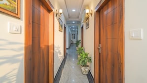 A hallway with wooden doors, potted plants, and wall-mounted light fixtures. - Fabhotel Broholic Stay Inn (Hyderabad)