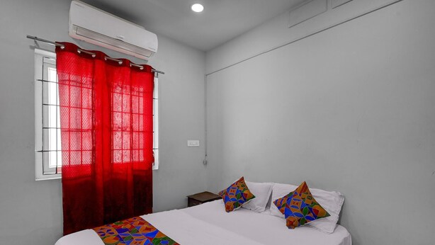 A bedroom with a bed, two pillows, a red curtain, and an air conditioning unit. - Fabhotel Pavis Inn (Chennai)