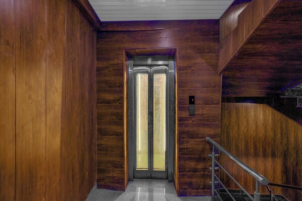 An elevator with a wooden interior and a metal handrail. - Fabhotel Vrishti Residency (Greater Noida)