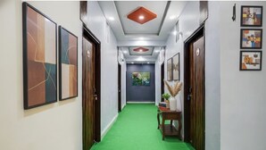 Un pasillo con alfombra verde, obras de arte enmarcadas en las paredes y una puerta de madera al final.