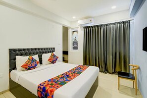 Una habitación de hotel con una cama grande, una silla, un ventanal con cortinas y un equipo de aire acondicionado.