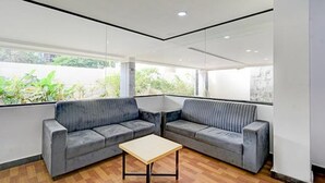 Una habitación moderna con dos sofás grises, una mesita de madera y amplias ventanas que dan a vistas de vegetación.