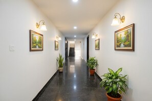 Un pasillo decorado con cuadros de paisajes, plantas en macetas e iluminación empotrada.