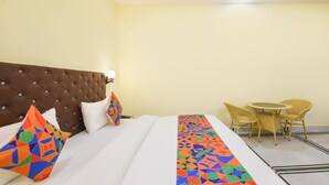 A hotel room with a tufted headboard, a bed with white bedding, colorful geometric pillows, a striped bed runner, and a small round table with chairs. - Fabhotel Rubicon (Faridabad)
