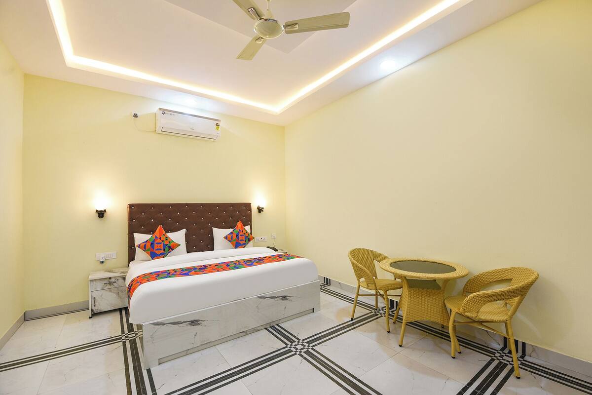 A hotel room with a bed, a ceiling fan, an air conditioner, a small table with chairs, and a patterned floor.