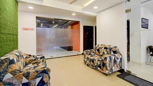 A modern interior with a ceiling fan, a reception area with a glass partition, and two patterned armchairs. - Fabhotel Jaswitha Grand (Hyderabad)