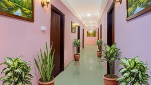 A hallway with pink walls, wooden doors, and potted plants. - Fabhotel Jaswitha Grand (Hyderabad)