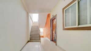 A narrow hallway with a staircase leading to an upper floor. The walls are plain with a single window on the right. - Fabhotel Yash Stay Inn (Bhopal)