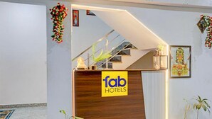 A hotel reception desk with a wooden finish and a 'fab hotels' sign. There are potted plants on either side of the desk. - Fabhotel Kashi (Varanasi)