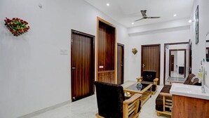 A modern living room with a sofa, a coffee table, and a wooden cabinet. There are two doors and a ceiling fan. - Fabhotel Kashi (Varanasi)