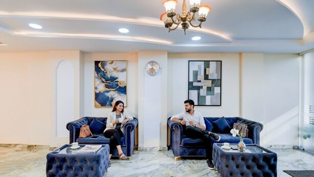A modern lobby with two dark blue sofas, a chandelier, and marble flooring. - Fabhotel Asian Heights (Hyderabad)