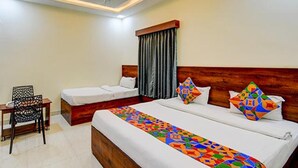 A hotel room with two beds, a wooden headboard, a ceiling fan, and a small table with a chair. - Fabhotel Asian Heights (Hyderabad)