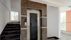 A modern elevator with a glass door, flanked by granite walls and a staircase. - Fabhotel High Rise Near Airport (Hyderabad)