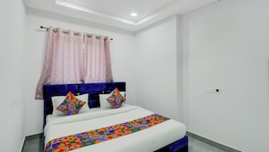 A neatly made bed with a geometric-patterned bedspread, a blue headboard, and pink curtains. - Fabhotel High Rise Near Airport (Hyderabad)