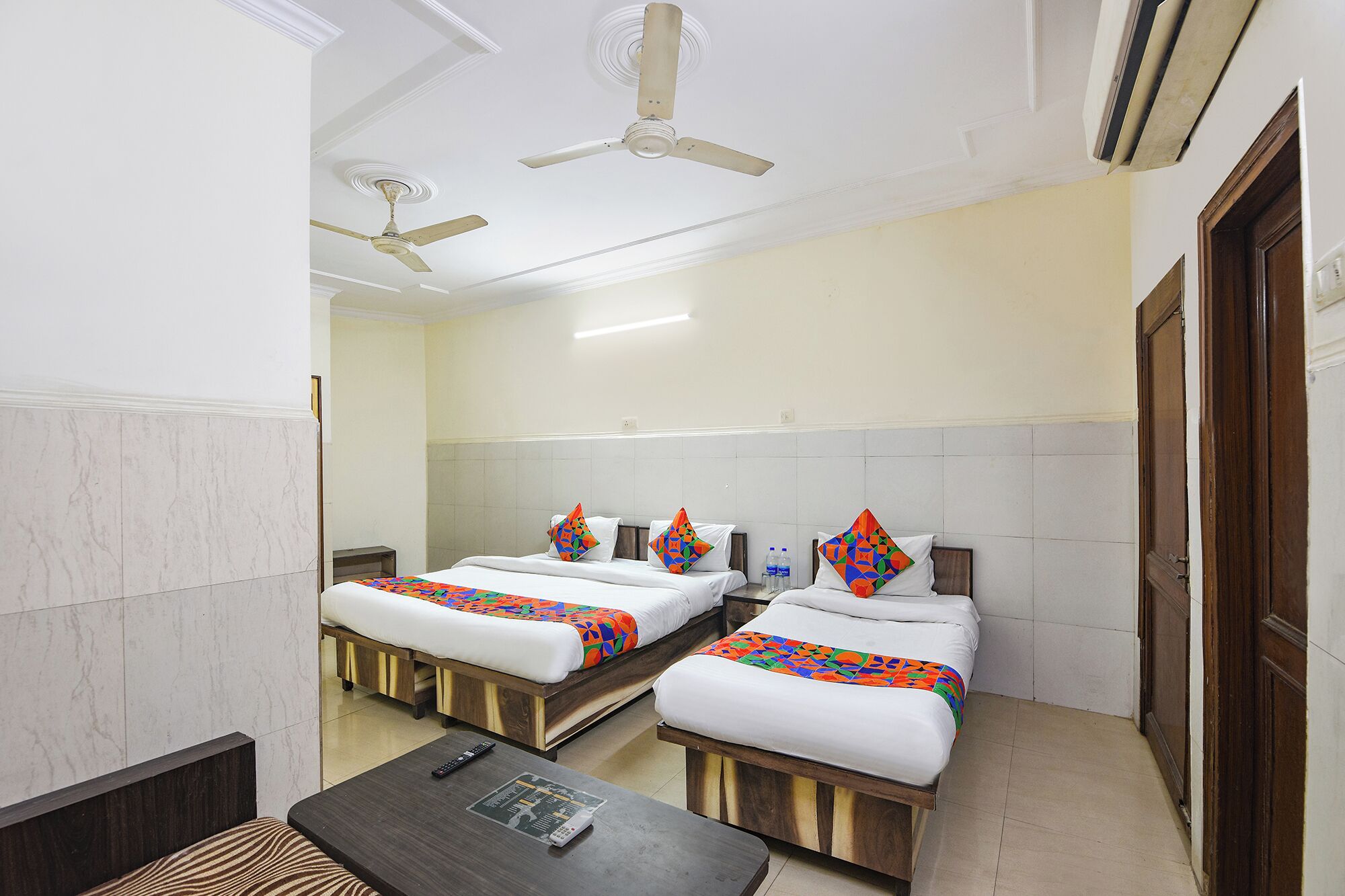 A hotel room with three single beds, a wooden nightstand, a small table, and two ceiling fans.