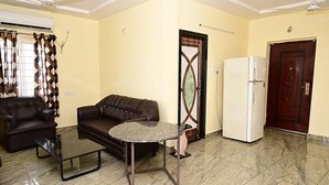 Un salón con sofá, una mesa de centro, un refrigerador y una puerta con diseño decorativo.