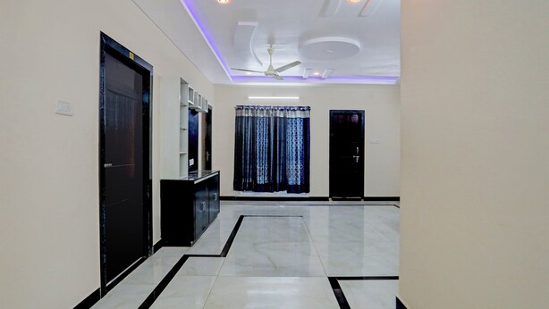 A hallway with a black and white tiled floor, a ceiling fan, recessed lighting, and a door on the left. - Fabexpress Coastal Suites (Kakinada)