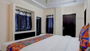 A hotel room with a bed, a ceiling fan, a TV, and a door. - Fabexpress Coastal Suites (Kakinada)