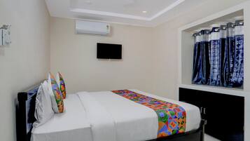 A hotel room with a bed, a flat-screen TV mounted on the wall, and a window with patterned curtains.