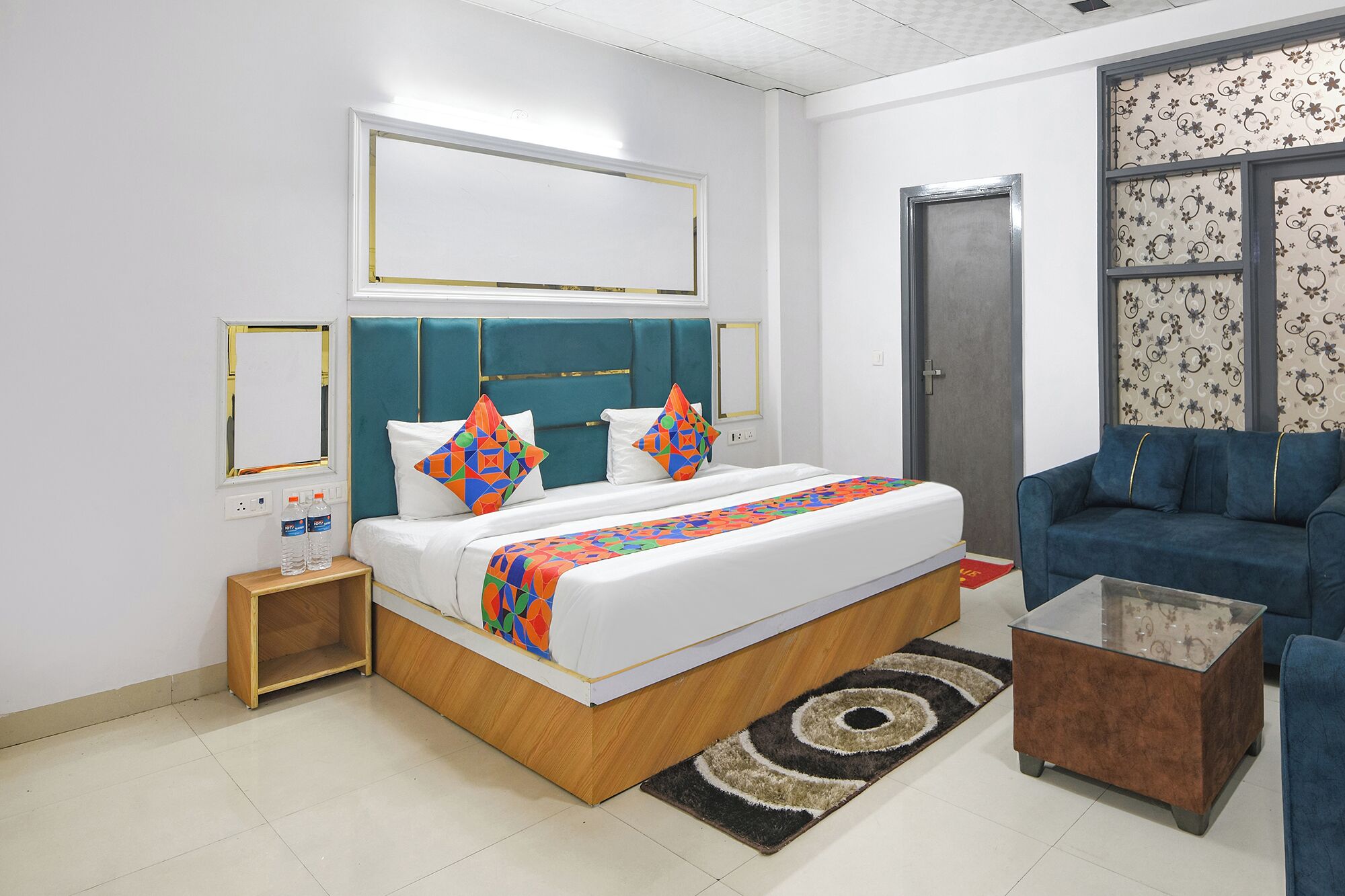 A hotel room with a bed, a blue sofa, a coffee table, and a patterned rug.