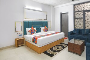A hotel room with a bed, a blue sofa, a coffee table, and a patterned rug. - Fabhotel Tulip Sarover Sector 18 (New Delhi)