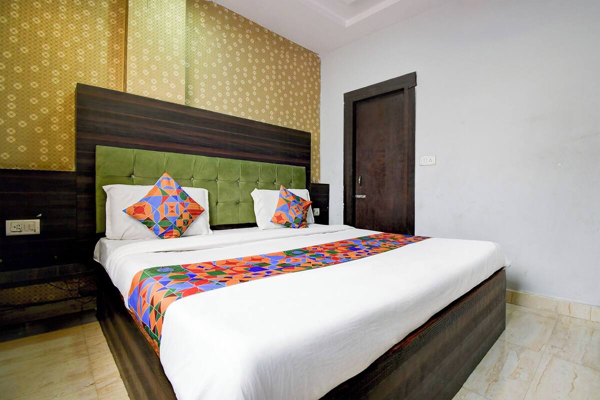 Une chambre d’hôtel avec un grand lit, une tête de lit recouverte d’un tissu vert, un papier peint à motifs et une porte en bois.
