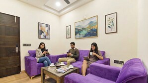Una habitación con sofás morados, una mesa de centro con tazas y una revista, y cuadros en las paredes.