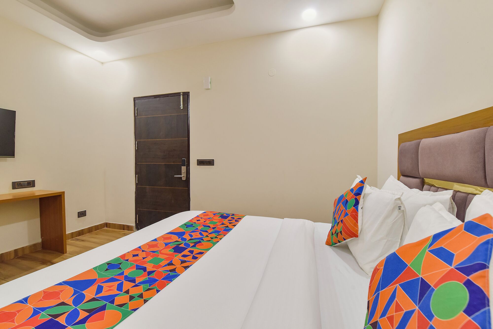 A hotel room with a bed, a wooden nightstand, a TV, and a door.