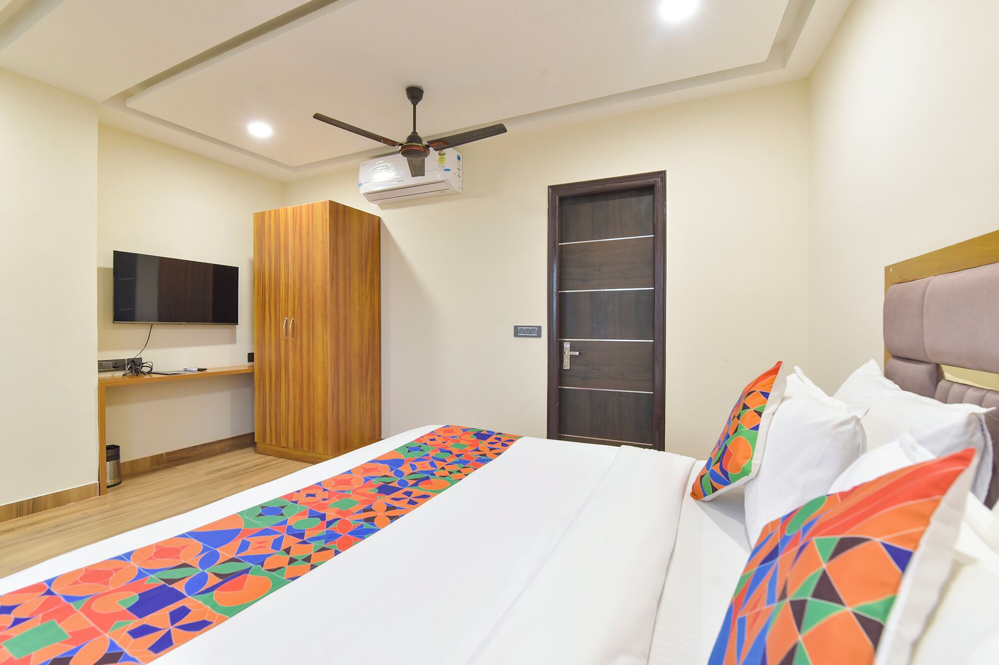 A hotel room with a bed, a wardrobe, a television, and a ceiling fan.