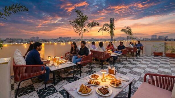Un espacio de comedor en la azotea con mesas y sillas, rodeado de vistas de la ciudad y un cielo al atardecer.