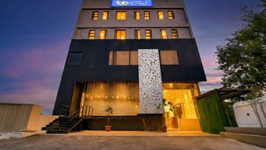 Un edificio moderno de hotel con techo plano, un letrero destacado que dice "fabHOTELS" y un panel decorativo vertical grande.