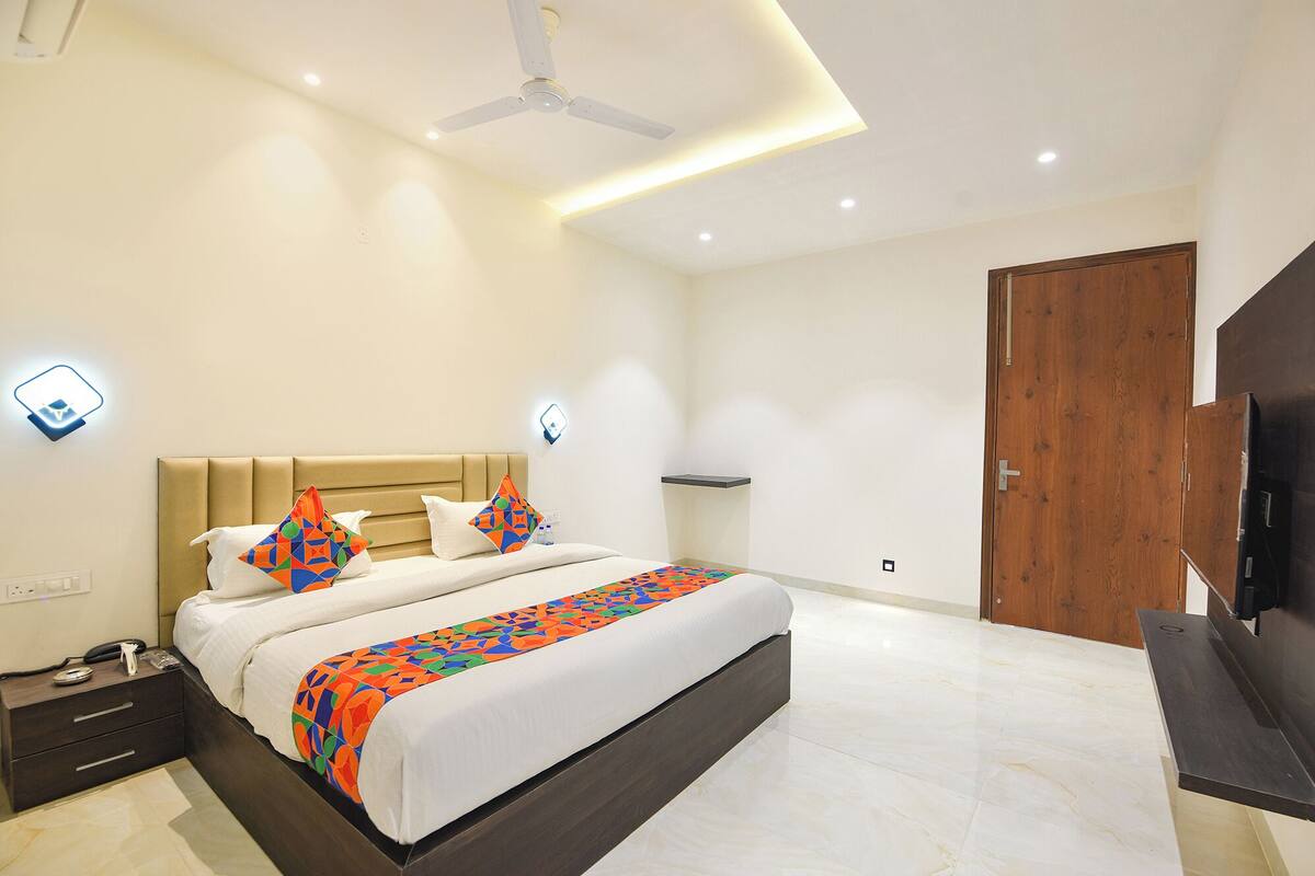 A modern hotel room with a large bed, a bedside table, a TV, and a ceiling fan.