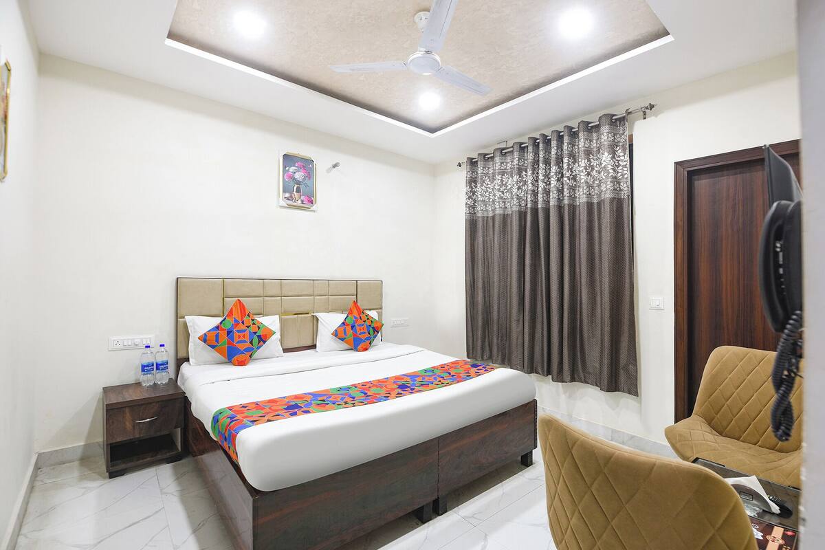 A hotel room with a bed, a bedside table, a chair, a ceiling fan, and a window with curtains.