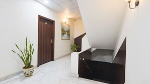 A hallway with a wooden door, a potted plant, a painting, and a staircase with a black handrail. - Fabhotel Canal View (Ludhiana)
