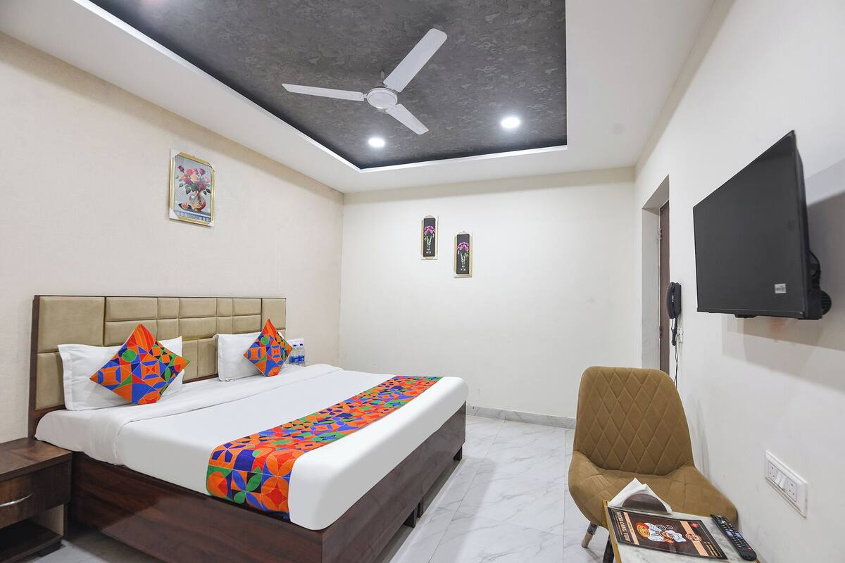 A hotel room with a bed, a chair, a TV, and a ceiling fan.