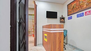 A hotel reception area with a wooden reception desk, a flat-screen TV mounted on the wall, and a painting depicting a cityscape. - Fabhotel Winsome Inn (Noida)