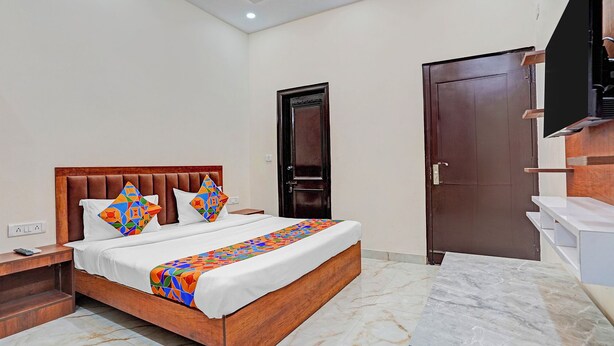A hotel room with a wooden bed, a nightstand, a desk, a wardrobe, and a TV mounted on the wall. - Fabhotel Winsome Inn (Noida)