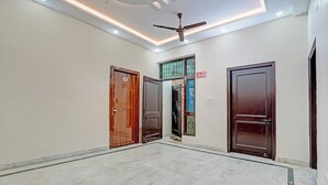 A hallway with three wooden doors, a ceiling fan, and a tiled floor. - Fabhotel Winsome Inn (Noida)