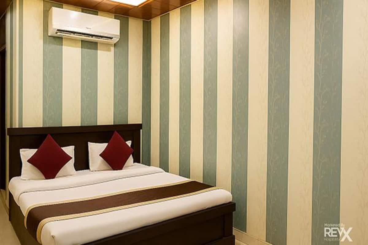 A hotel room with a bed, striped wallpaper, and an air conditioning unit.