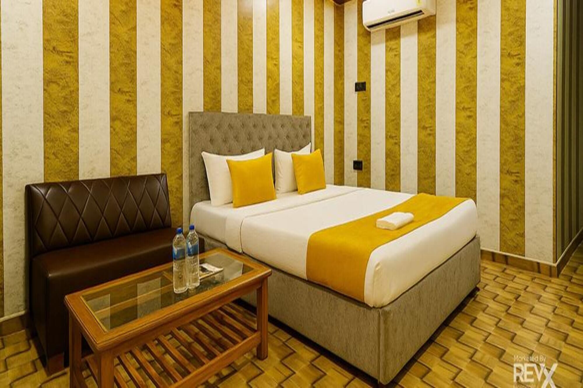 A hotel room with a bed, a sofa, a glass-top coffee table, and a patterned floor.