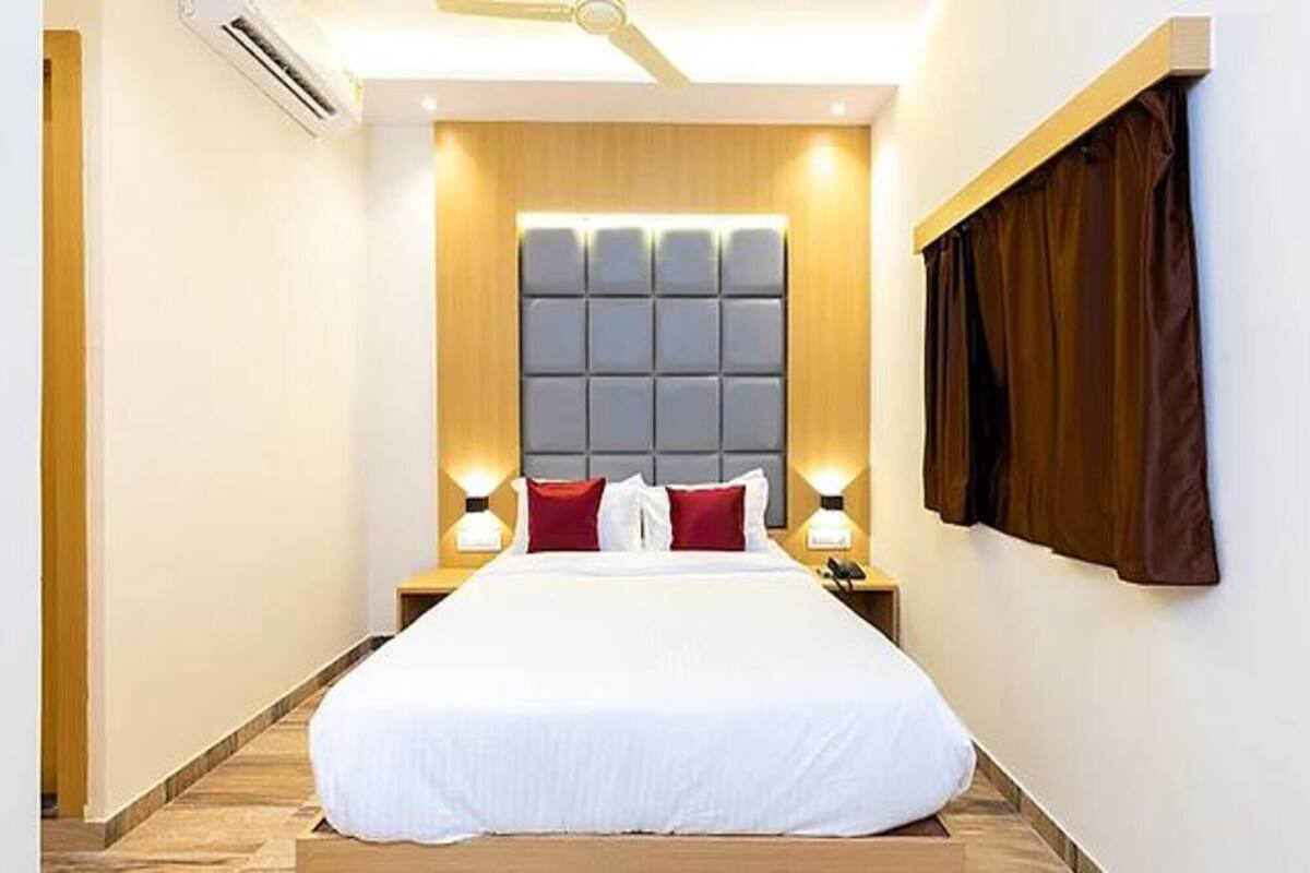 A hotel room with a large bed, a headboard with a padded design, two bedside lamps, and a window with curtains.
