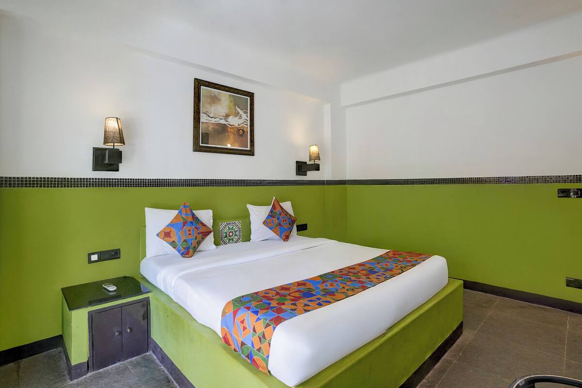 A hotel room with a green accent wall, a bed with patterned bedding, two wall-mounted lamps, and a framed picture above the bed.